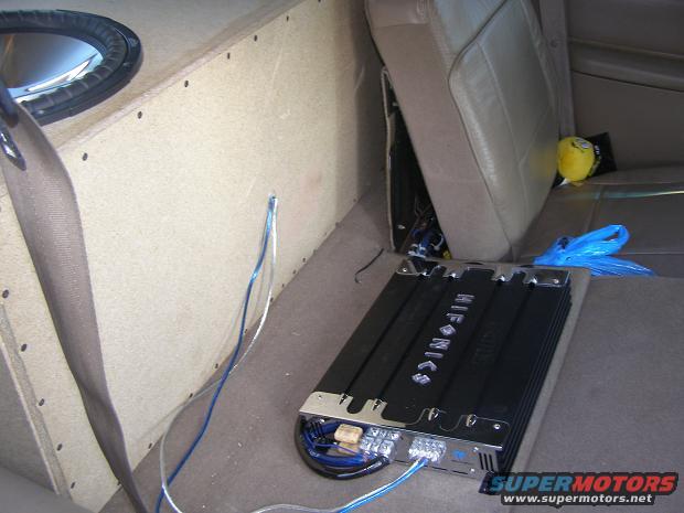 Car interior showing a subwoofer box, amplifier, and leather seats