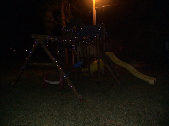 Wooden swing set decorated with colorful Christmas lights at night