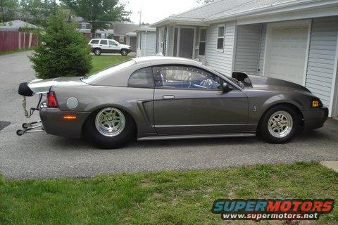Gray drag car with large rear spoiler and hood scoop, side view