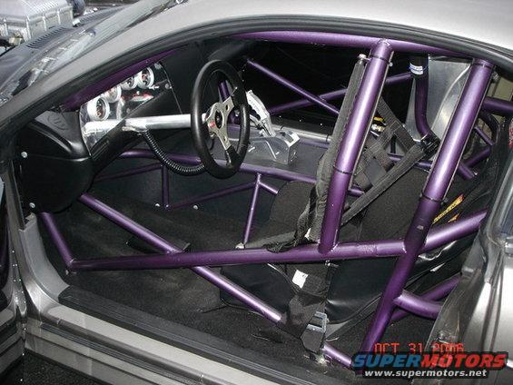 Car interior with purple roll cage, racing seats, and aftermarket steering wheel. Date stamp visible