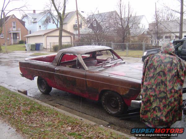 Rusty 1967 Ford Ranchero parked on a wet street, seen from the front passenger side