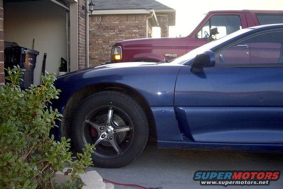 Side view of a blue 1994 Dodge Stealth parked next to a red pickup truck
