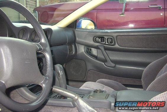 Interior view of a 1994 Dodge Stealth showing the steering wheel, dashboard, center console, and door panel. Another vehicle is visible through the window