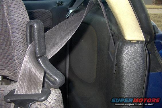 Car interior showing a gray seatbelt and patterned seat fabric. A black plastic trim piece is visible