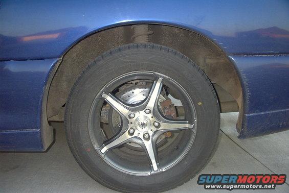 Close-up of a blue car's front wheel and fender, showing aftermarket rims and drilled brake rotors