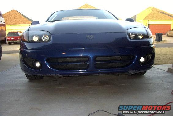 Front view of a blue sports car with its headlights and fog lights on. The car has a Dodge emblem on the hood