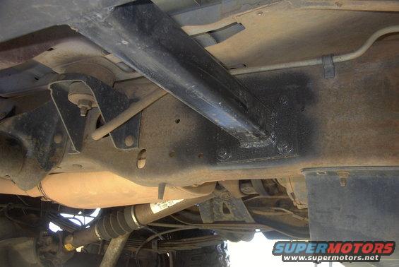 Undercarriage of a vehicle showing frame rails, suspension components, and exhaust system. A label is partially visible