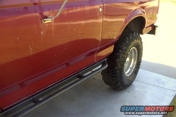 Red SUV side door with scratches and a black slider bar below. Large off-road tire visible