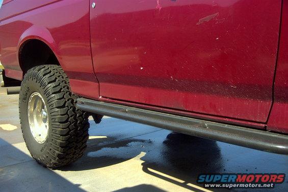 Side view of a red SUV, likely a 1992 Ford Bronco, showing its large off-road tire and black running board