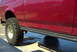 1994 Ford Bronco - Close-up side view of a red SUV, a large tire and a black running board.