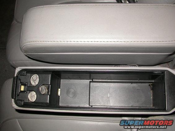 Gray leather armrest above open car storage compartment with coins inside
