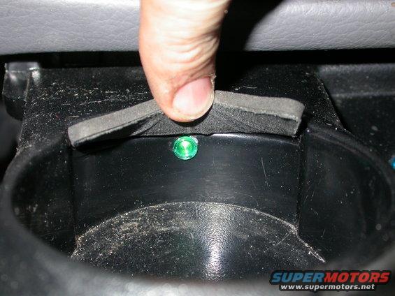 Cup holder interior with a finger pressing a foam piece over a green illuminated light