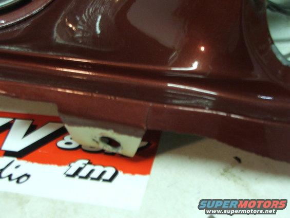 Close-up of a dark red car part showing a paint chip on a white tab. Text from a sticker is visible underneath
