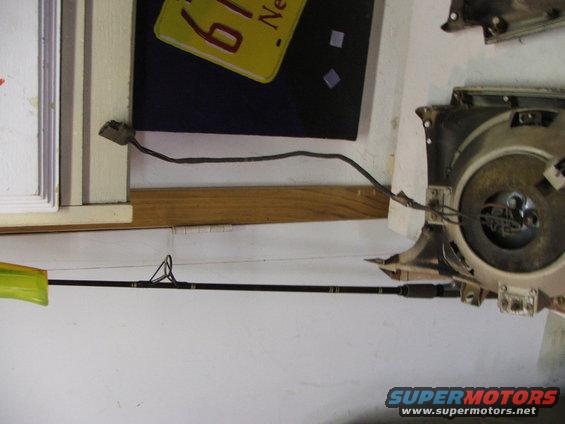 Car headlight assembly with wires and a fishing rod leaning against the wall