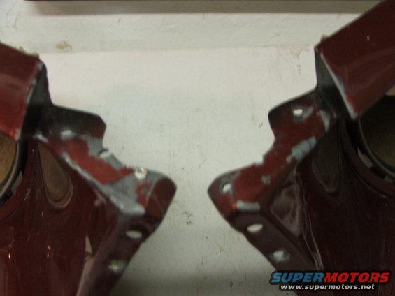 Two red metal car fender mounting brackets with chipped paint