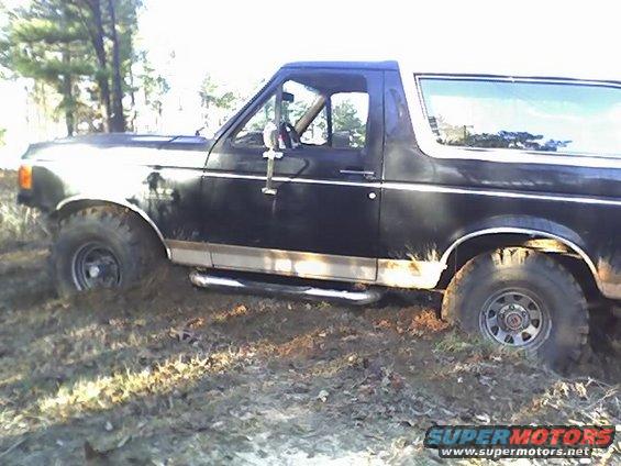 Black Ford Bronco stuck in mud, side view. Looks like a 1987 model
