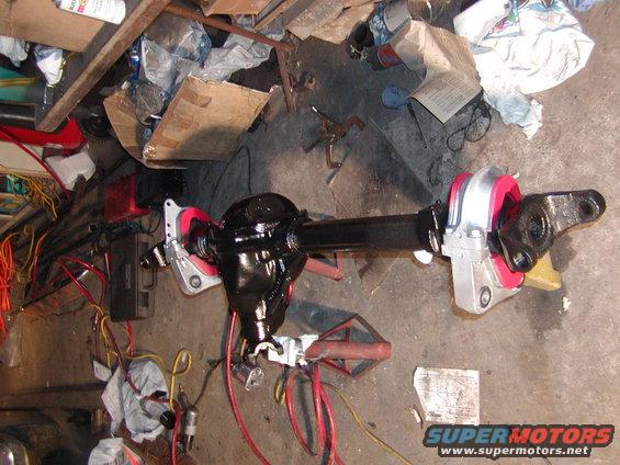Differential axle assembly with black housing and red and silver mounting brackets, on a concrete floor with tools and debris