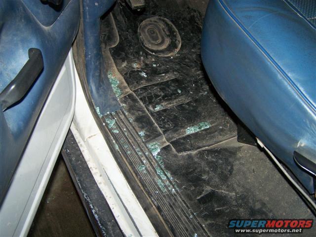 Interior shot of a vehicle showing broken glass on the floor near the driver's seat and door