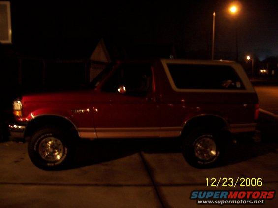Red Ford Bronco with a white top, side view, parked at night