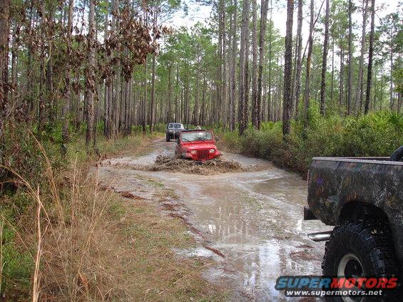 Red Jeep Wrangler splashing through mud on a wooded trail