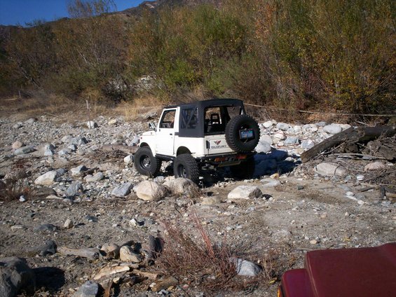 White 1987 Suzuki Samurai with soft top parked on rocky terrain. Spare tire mounted on rear