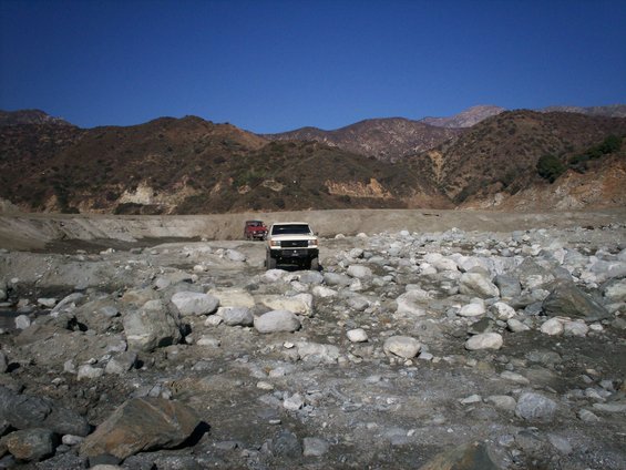 White off-road vehicle and red off-road vehicle on rocky terrain with mountains in background