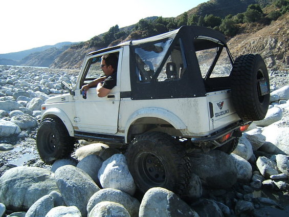 White Suzuki Samurai with soft top navigating a rocky riverbed