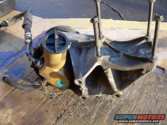 Power steering pump with reservoir and hoses attached, mounted on a bracket with bolts