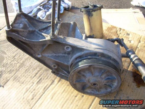 Power steering pump assembly with pulley and reservoir, metal and plastic components, on cardboard