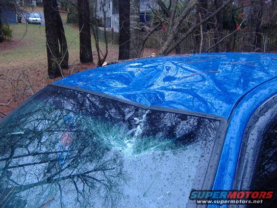 Blue car's roof is dented and windshield is cracked. Another car is visible in the background