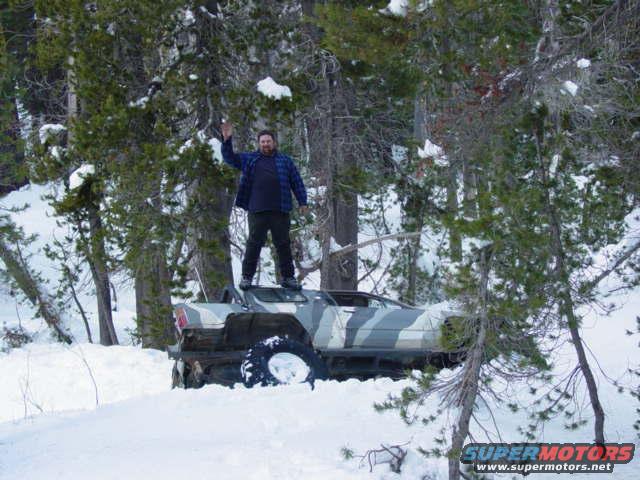 Camouflaged SUV stuck in snow with a man waving from its roof