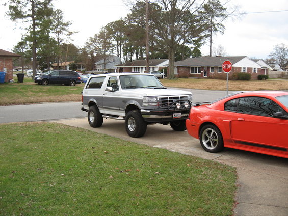1994 Ford Bronco parked next to a red Ford Mustang in a driveway