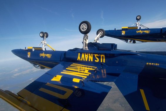 Two blue jets with landing gear down in flight, one labeled "U.S. NAVY" and "Blue Angels"