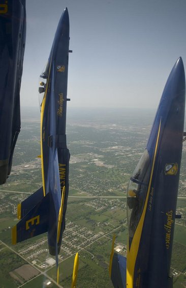 Three Blue Angels jets flying in formation over a suburban landscape