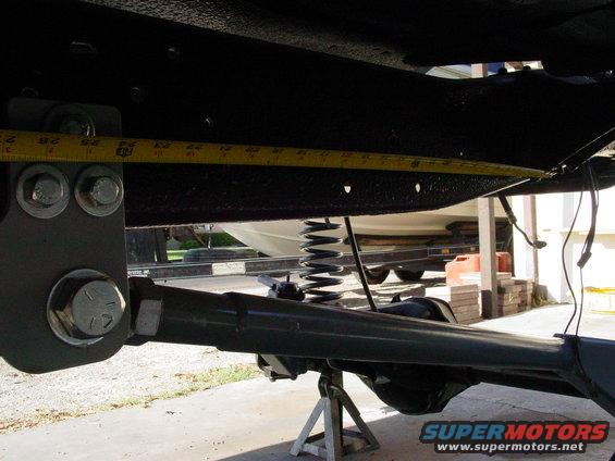 Measuring suspension component with a yellow tape measure. Boat on trailer in background