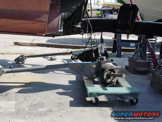 Vehicle chassis and suspension parts on dollies, with a maroon door in the background