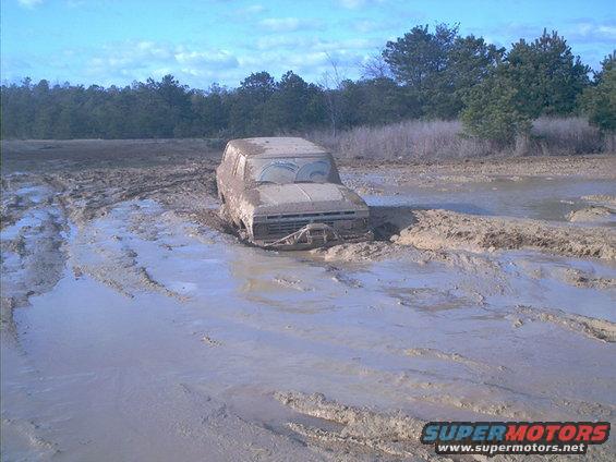SUV stuck deep in a mud pit with trees in background. Water and mud everywhere