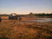 1978 Ford Bronco - Tow truck is stuck in a muddy field with water and trees visible in the distance.