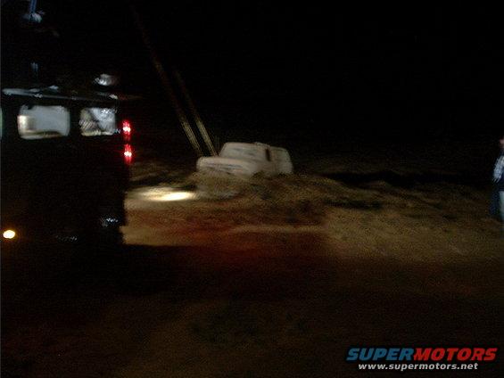 White SUV partially buried in dirt at night, with a tow truck in the foreground