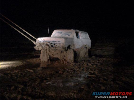 White SUV stuck deep in mud at night, with tow ropes attached to the front