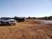 1978 Ford Bronco - A white Ford Excursion and a military truck are parked in a muddy, open field under a clear blue sky.