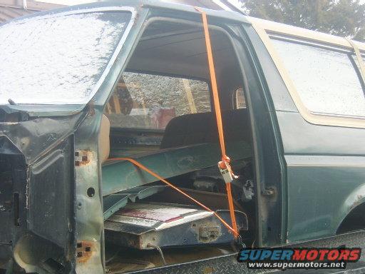 Green Ford Bronco with tan top, door open, strapped to a trailer, showing interior and some rust