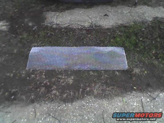 Rectangular piece of silver mesh, likely a car grille insert, lying on the ground