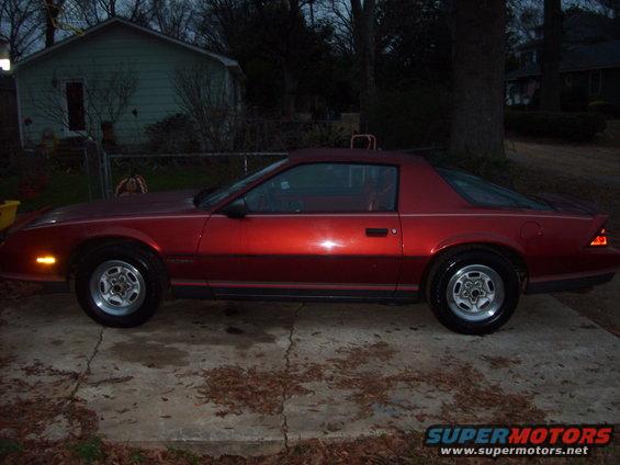 Red coupe parked on concrete driveway, house and trees in background