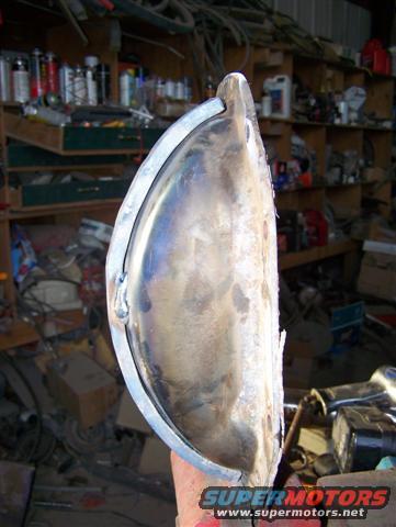 Metal part with curved edge held by hand, workshop background