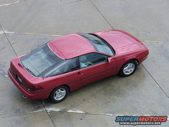 Red coupe from a high angle, showing its side and front quarter. The car has a large glass rear hatch and a sunroof