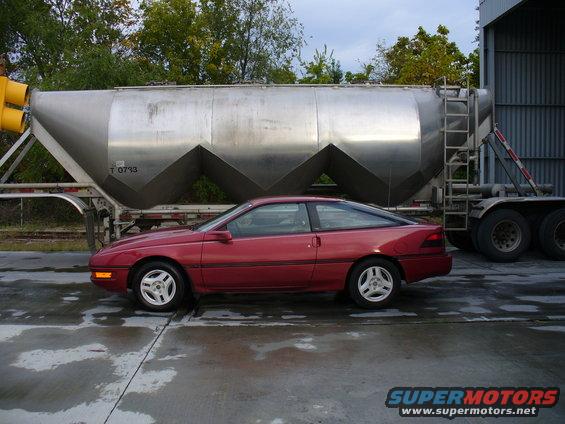 Red 1991 Ford Probe coupe parked next to a silver tanker trailer