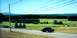 1997 Ford Crown Victoria - A dark sedan drives down a road in a rural landscape under a bright blue sky.