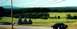 1997 Ford Crown Victoria - A black sedan is visible on a road with a wooded landscape in the background.