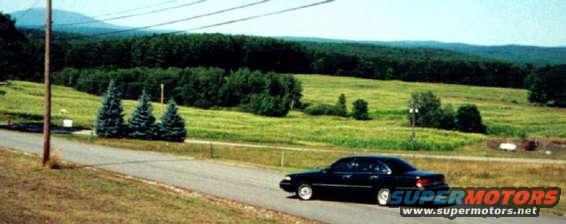Black 1997 Ford Crown Victoria driving on a rural road with green hills in the background
